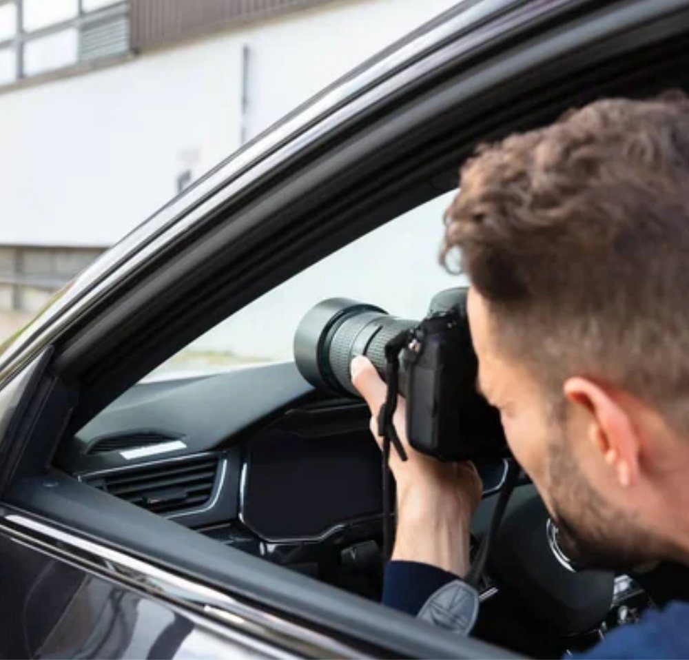 Professional surveillance investigator discreetly monitoring from inside a vehicle with a camera